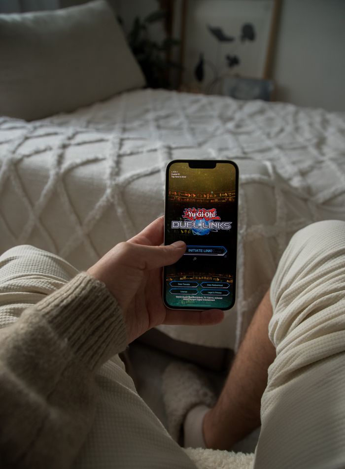 about-01 Hand holding smartphone in a cozy bedroom, displaying a gaming app.