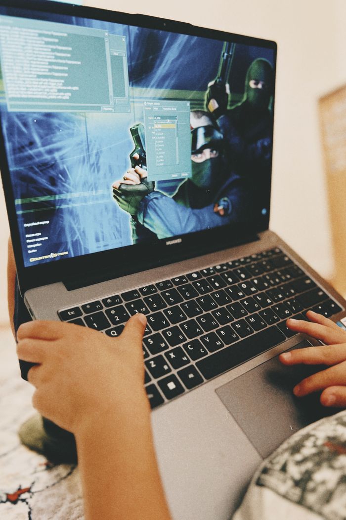 Child focused on playing a shooter video game on a laptop indoors.