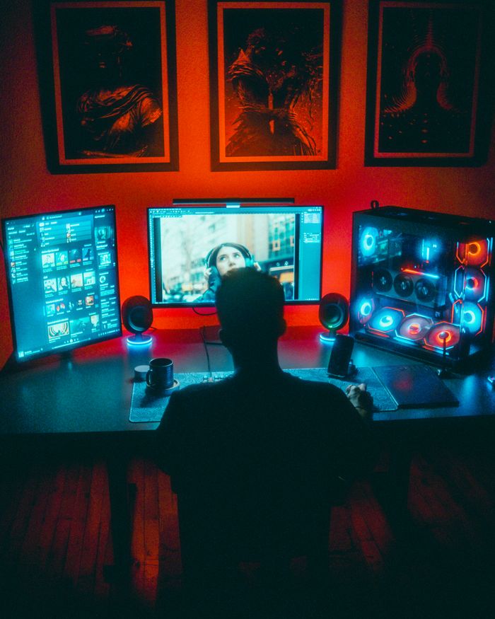 A gamer engrossed in a vibrant RGB computer setup with dual monitors at night.