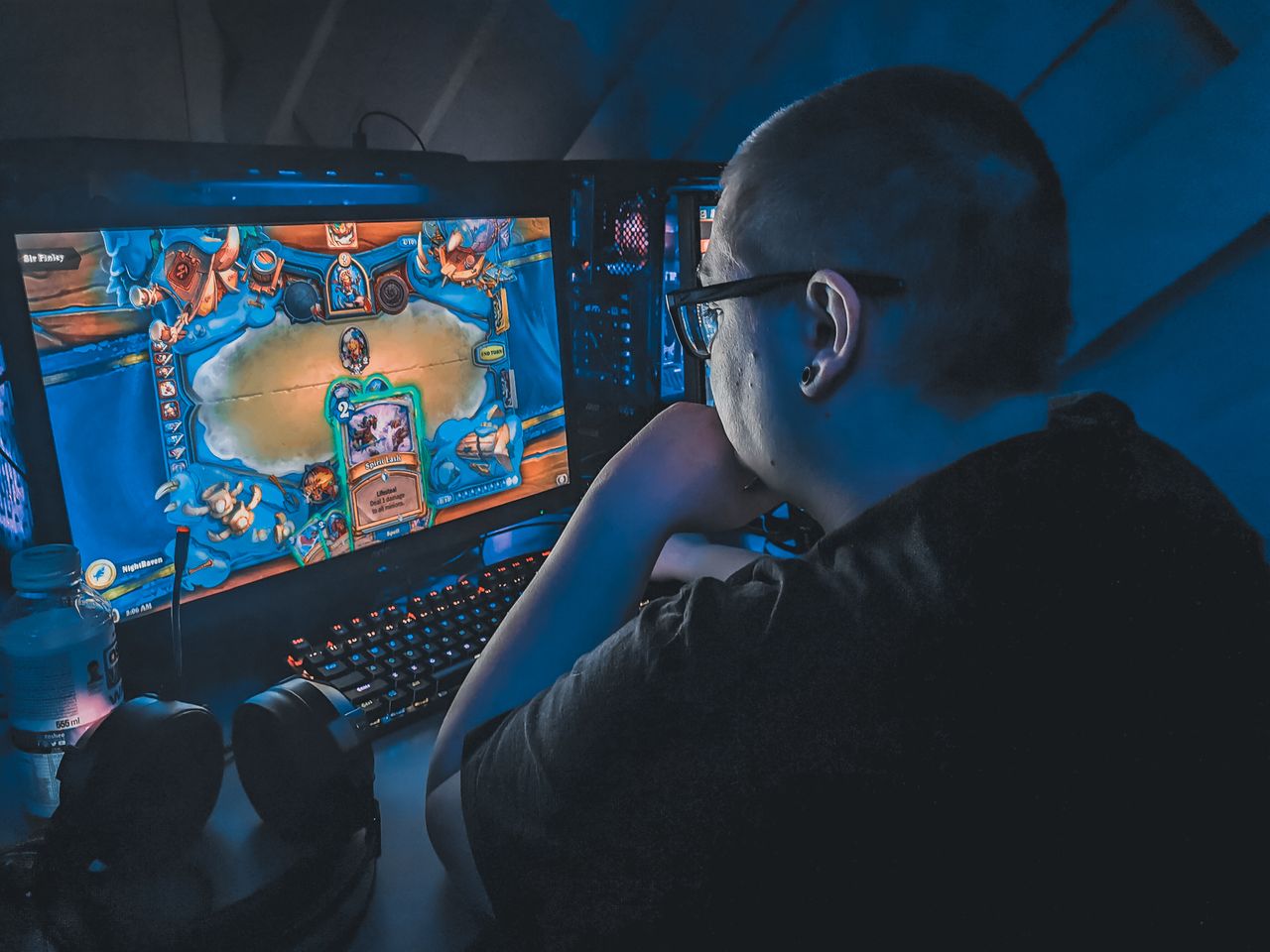 High angle of plump male gamer thinking and playing video game while sitting at table under blue light
