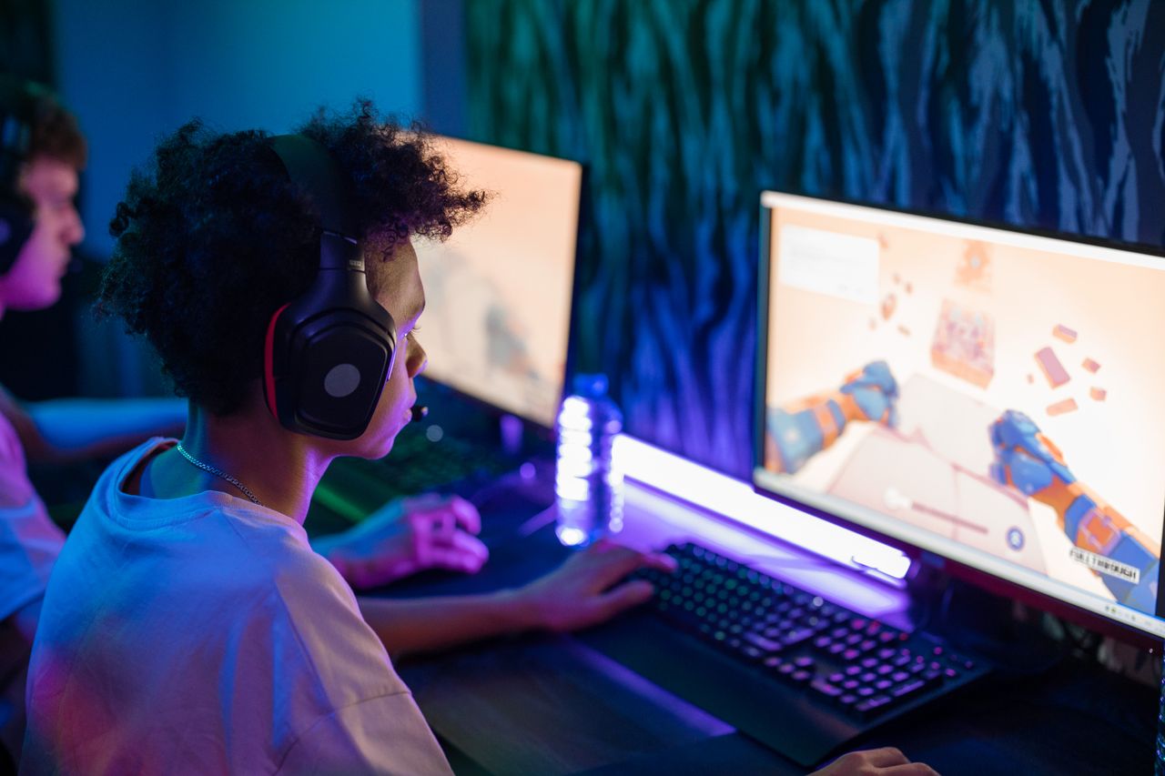 about-hero-img Teen gamers engrossed in online computer game in a vibrant, modern gaming room.